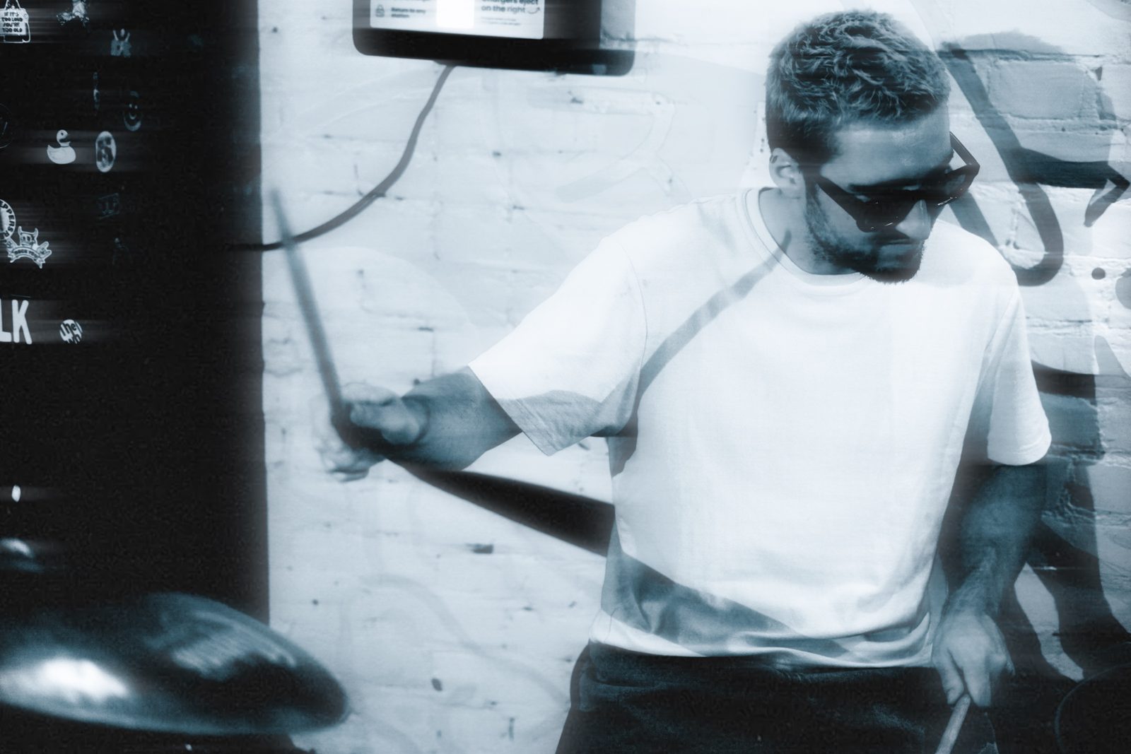 Flozinho playing drums against a white brick wall